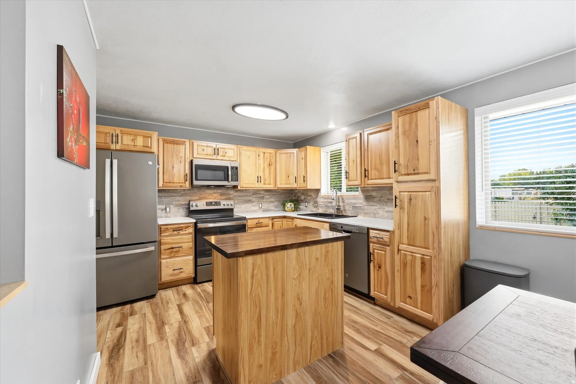 Kitchen featuring wood-finish flooring, natural wood cabinetry, stainless steel appliances, and a central island with a contrasting countertop