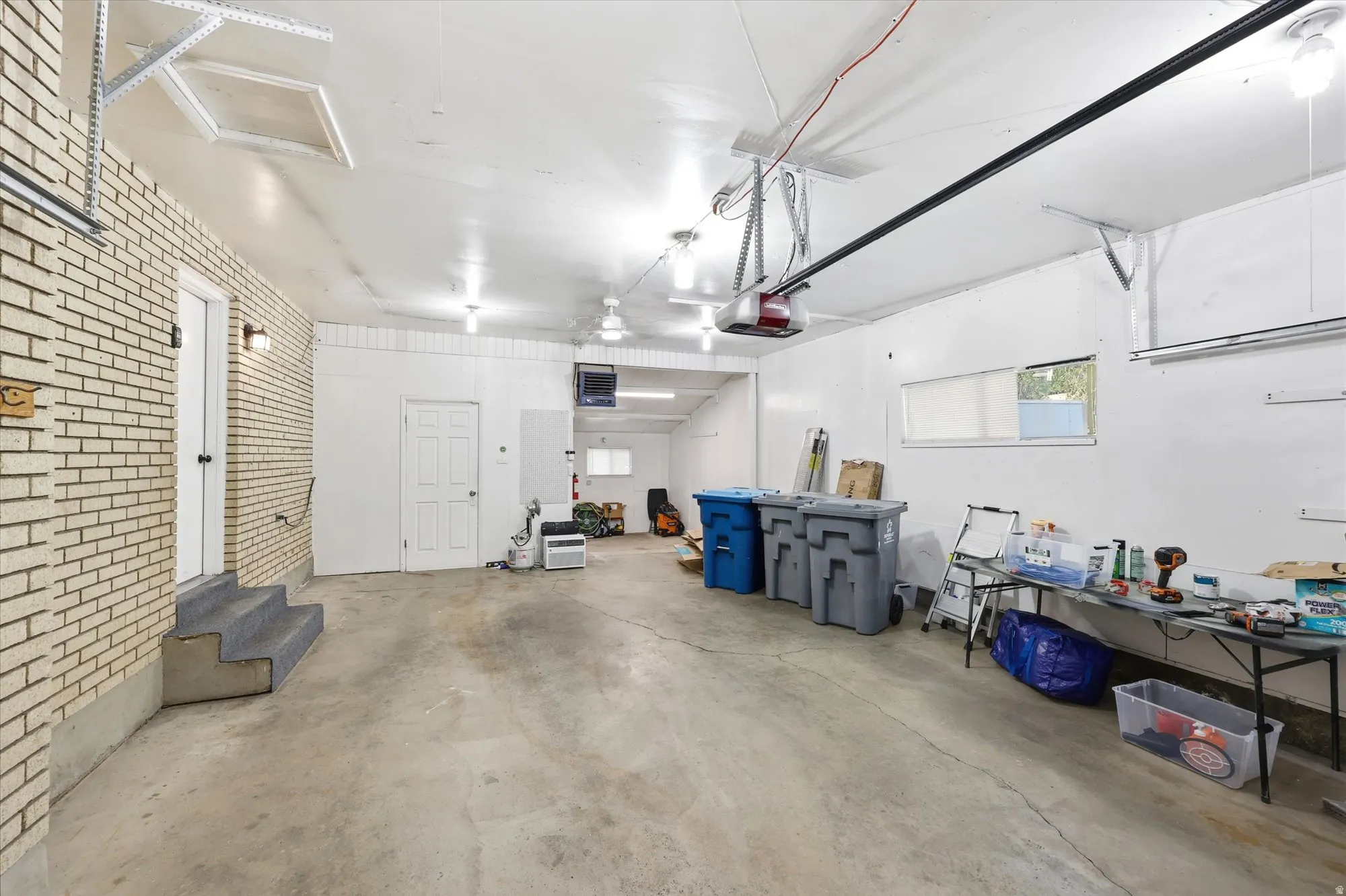 Spacious garage with concrete flooring, exposed brick wall, and multiple entry points