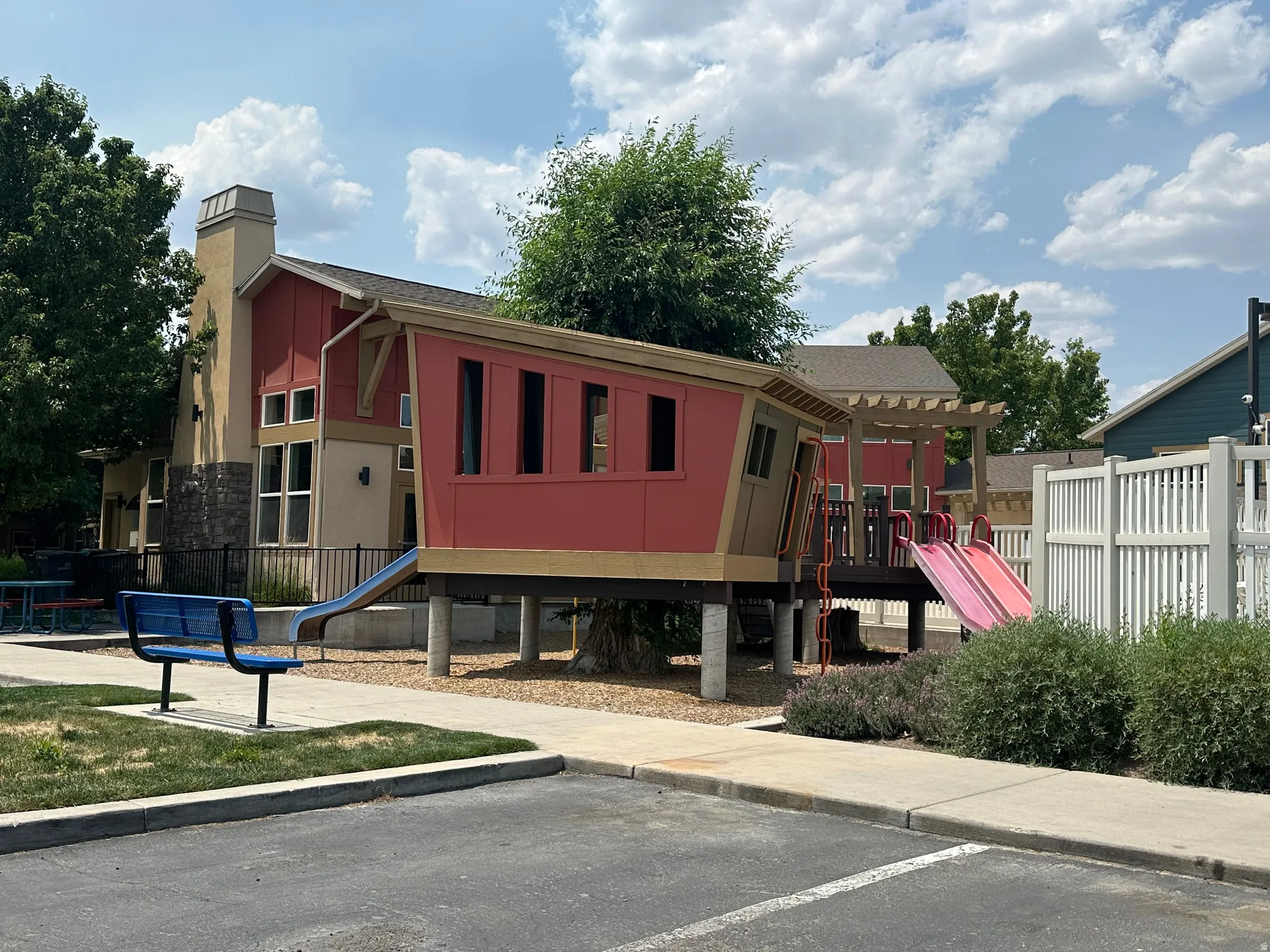 Community playground area featuring a play structure with red siding, multiple slides, and a pergola-covered deck