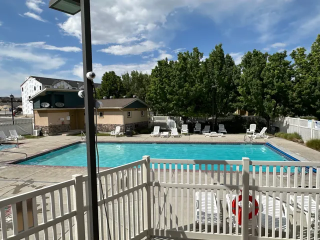 Outdoor swimming pool featuring a concrete deck, white perimeter fencing, and mature trees providing natural screening