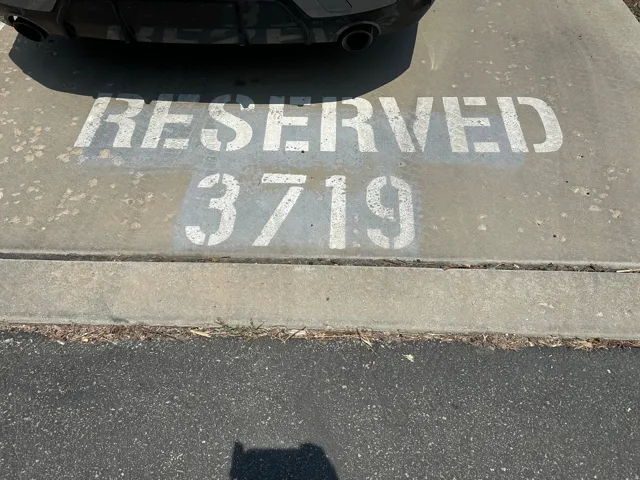 Reserved parking space with stenciled numbering on concrete, featuring a defined curb separating it from an asphalt surface