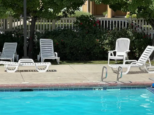 Swimming pool with concrete decking, perimeter landscaping, and a white picket fence backdrop