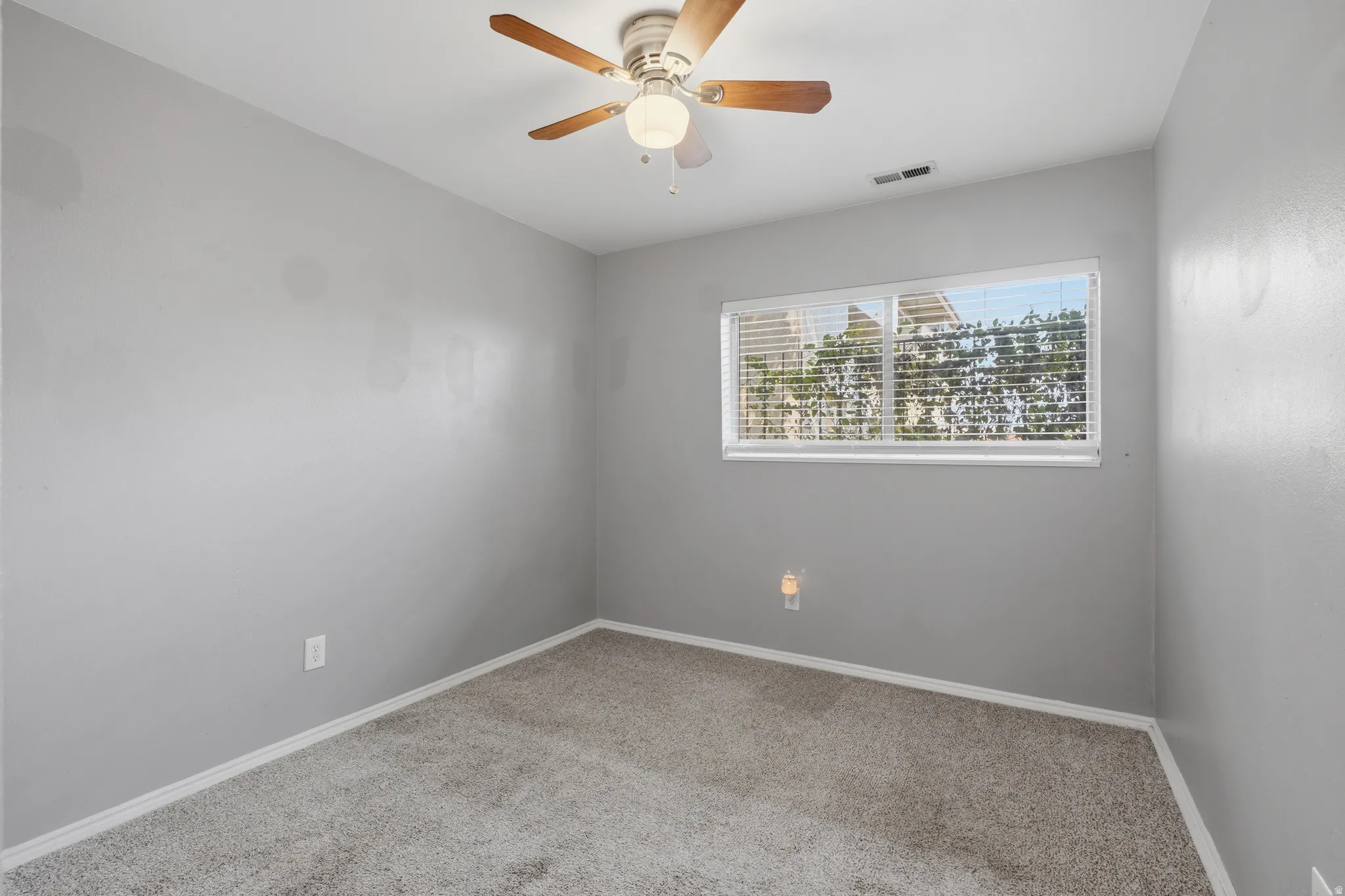 Carpeted room featuring a ceiling fan with integrated lighting, a rectangular window with horizontal blinds, and baseboard trim