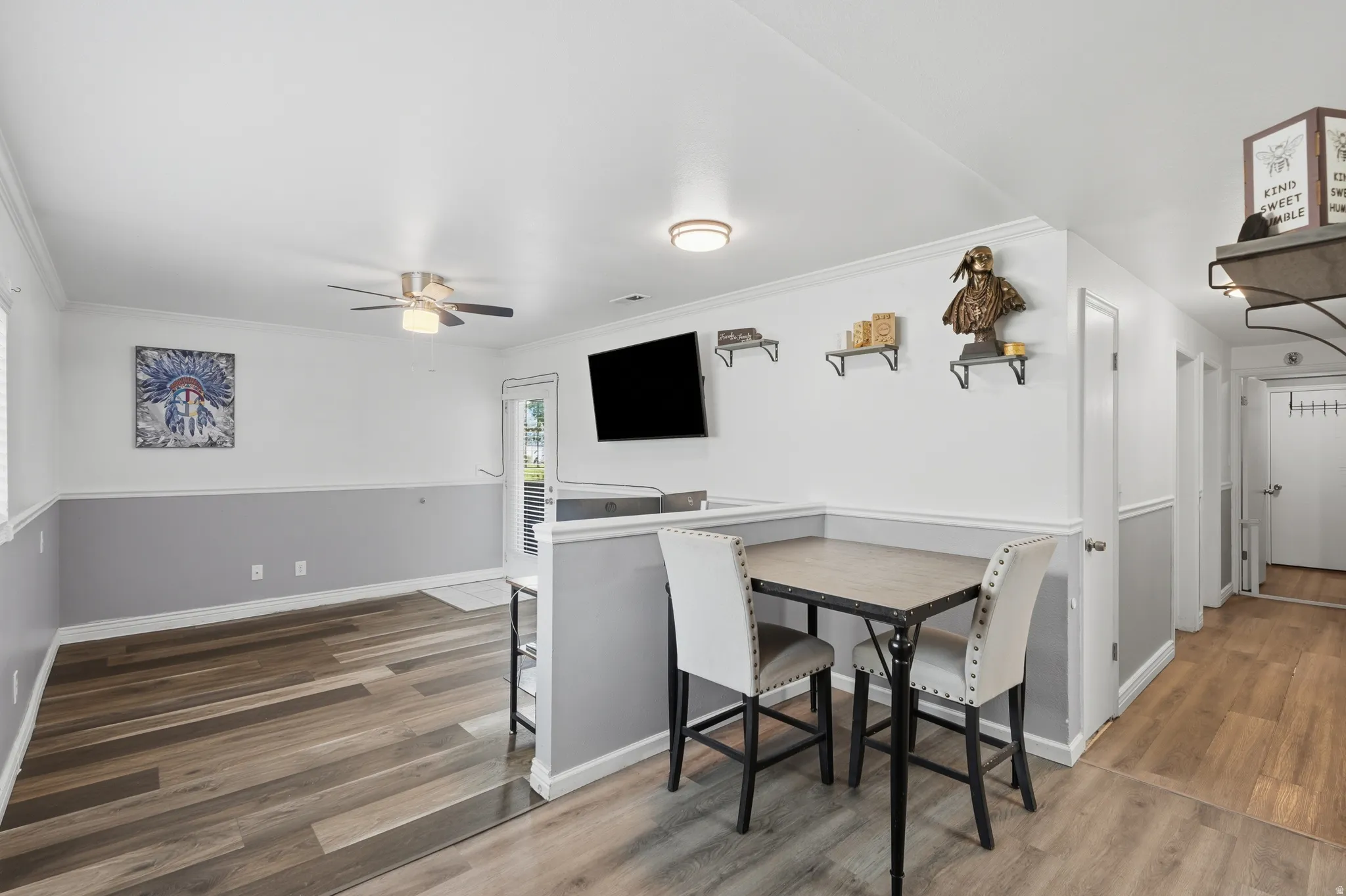 Open-concept living space with wood-finish flooring, white walls, and a grey wainscoting accent