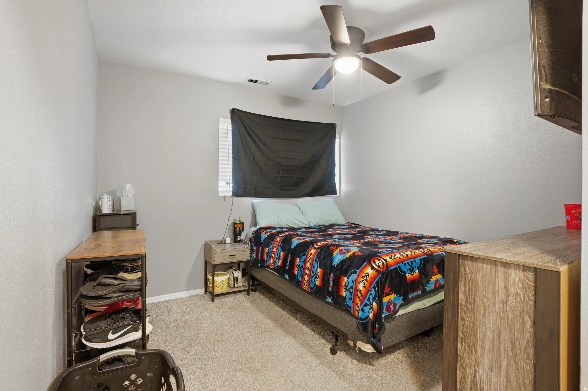 Carpeted bedroom with a ceiling fan, window with blinds, and light gray wall paint