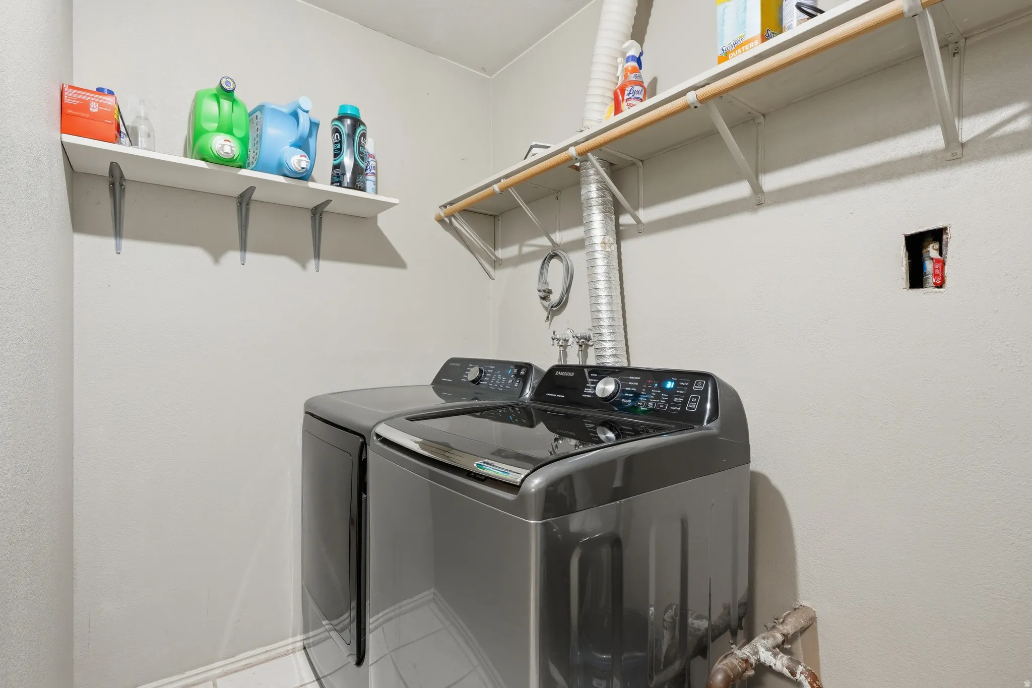 Dedicated laundry area featuring a washer and dryer, tile flooring, and two wall-mounted storage shelves