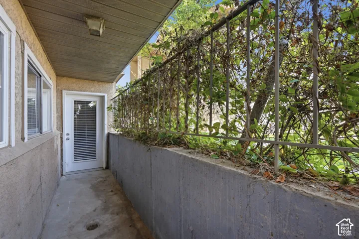 Private outdoor corridor featuring a security gate with established greenery, a secure entry door with integrated blinds, and an overhead light fixture