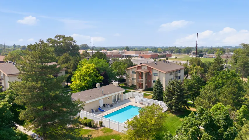 Outdoor swimming pool surrounded by a white picket fence, adjacent to a clubhouse building with a shingled roof