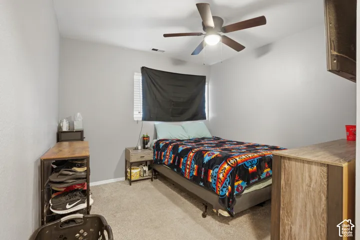Carpeted bedroom with a ceiling fan, window with blinds, and light gray wall paint