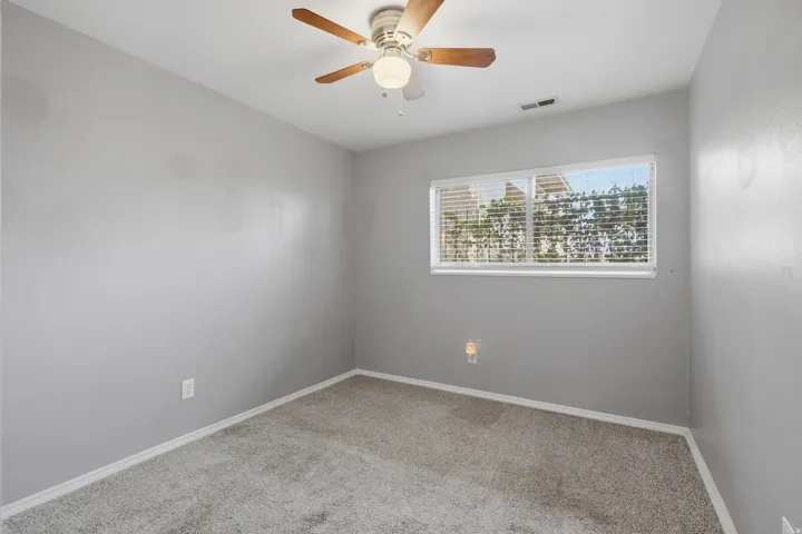 Carpeted room featuring a ceiling fan with integrated lighting, a rectangular window with horizontal blinds, and baseboard trim