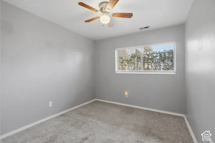 Carpeted room featuring a ceiling fan with integrated lighting, a rectangular window with horizontal blinds, and baseboard trim