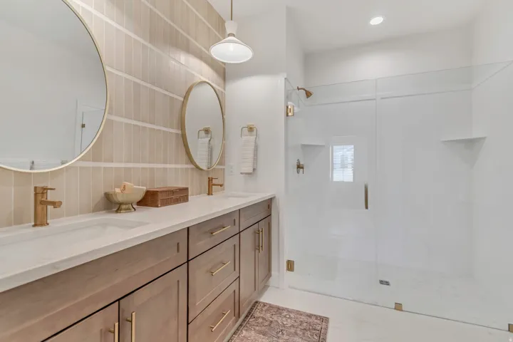 Double vanity featuring neutral wood-finish cabinetry, white countertops, and circular mirrors