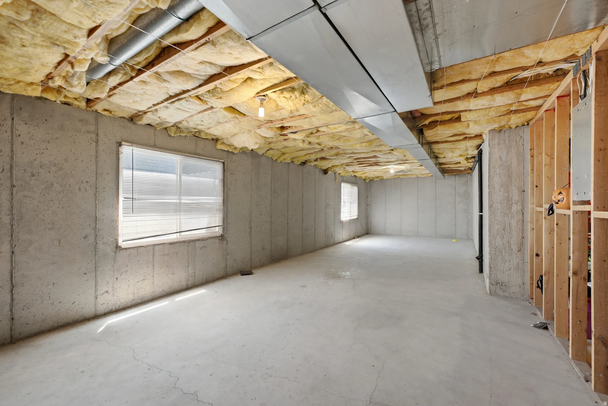 Unfinished basement with concrete walls, exposed insulation, ductwork, and two visible windows