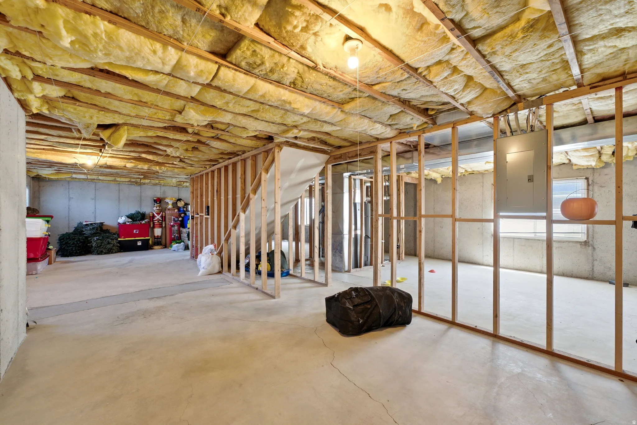 Unfinished lower level featuring concrete flooring, exposed ceiling insulation, and visible wood framing for potential expansion