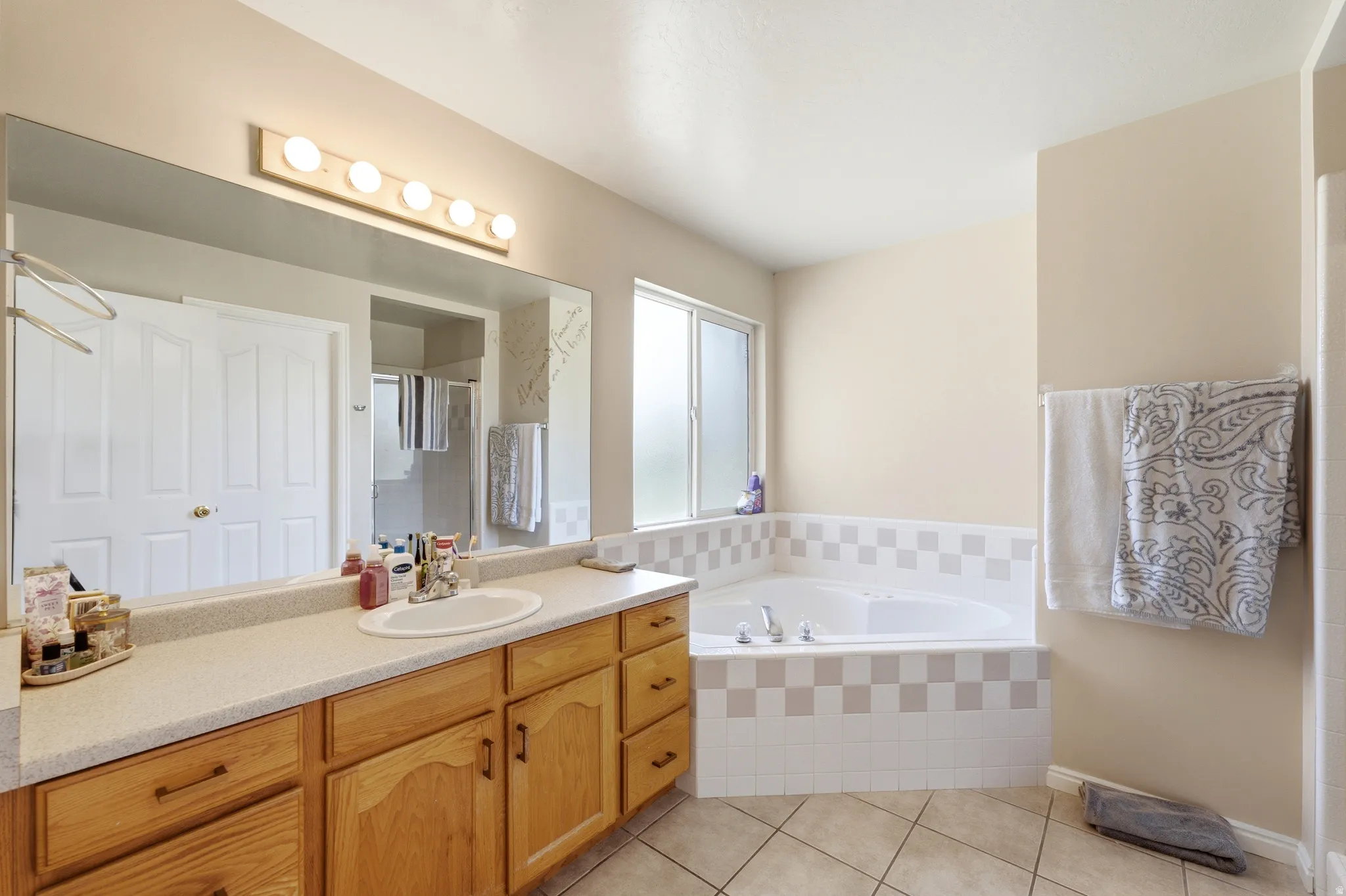 Bathroom featuring a large corner soaking tub with tiled surround, wood-finish vanity with ample counter space, integrated sink, and oversized wall mirror