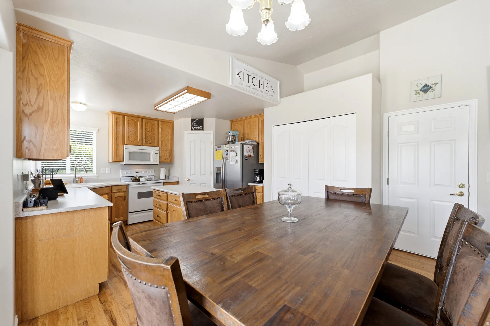 Open-concept kitchen and dining area featuring vaulted ceilings, light wood-finish cabinetry, white appliances, and wood-finish flooring