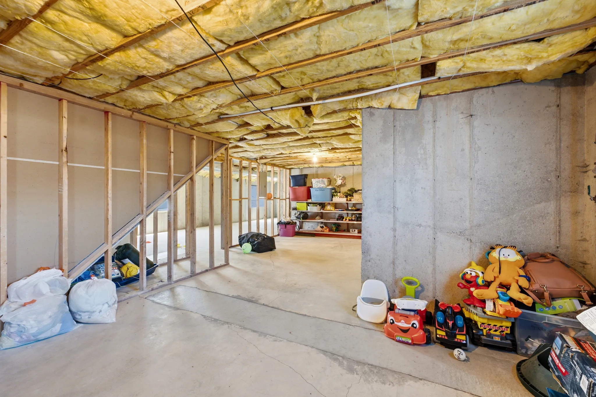 Unfinished basement featuring exposed concrete walls, wood framing, visible insulation, and concrete flooring