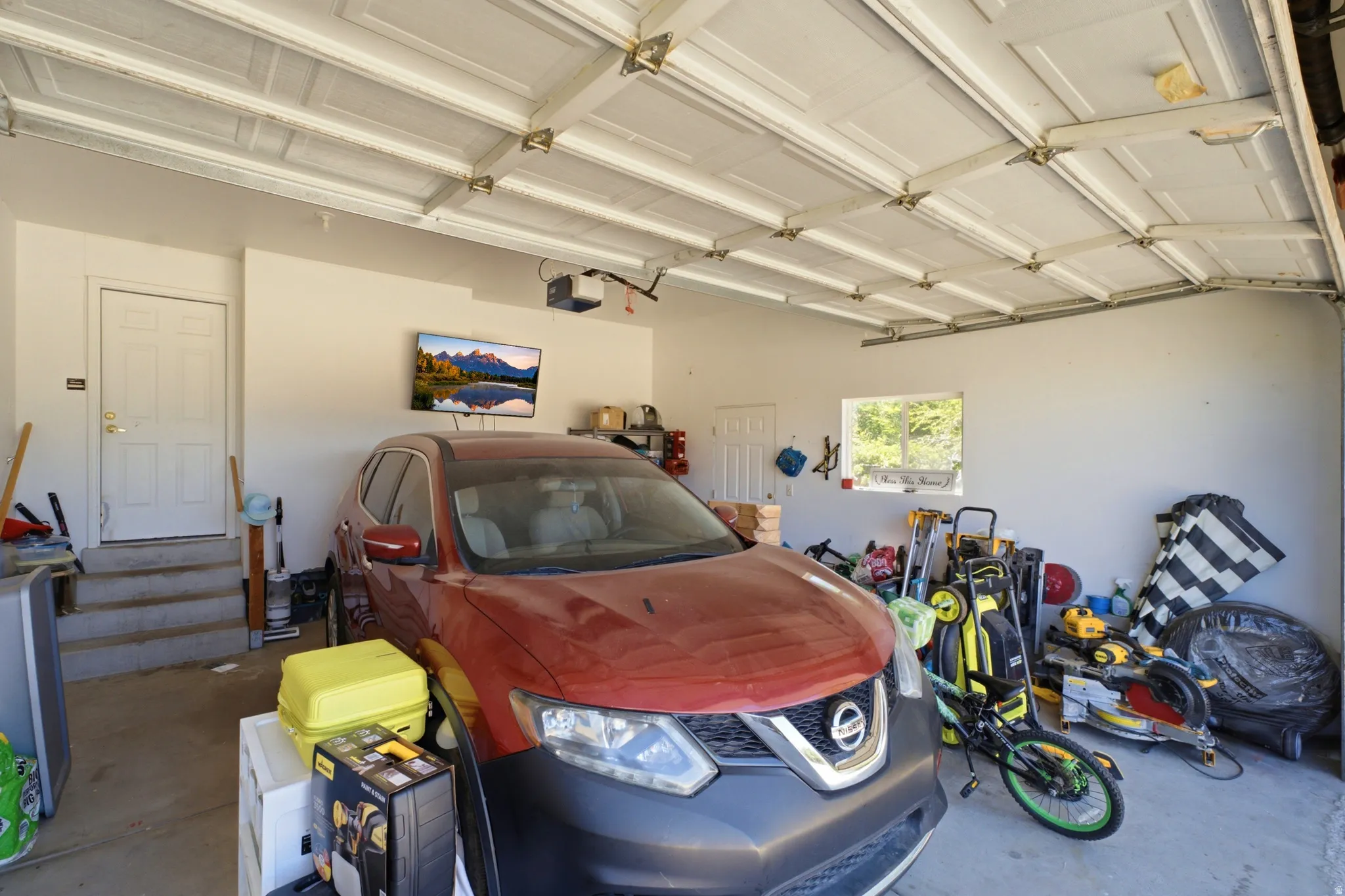 Spacious garage featuring white paneled overhead doors, a built-in window, an interior access door with steps, and an overhead garage door opener