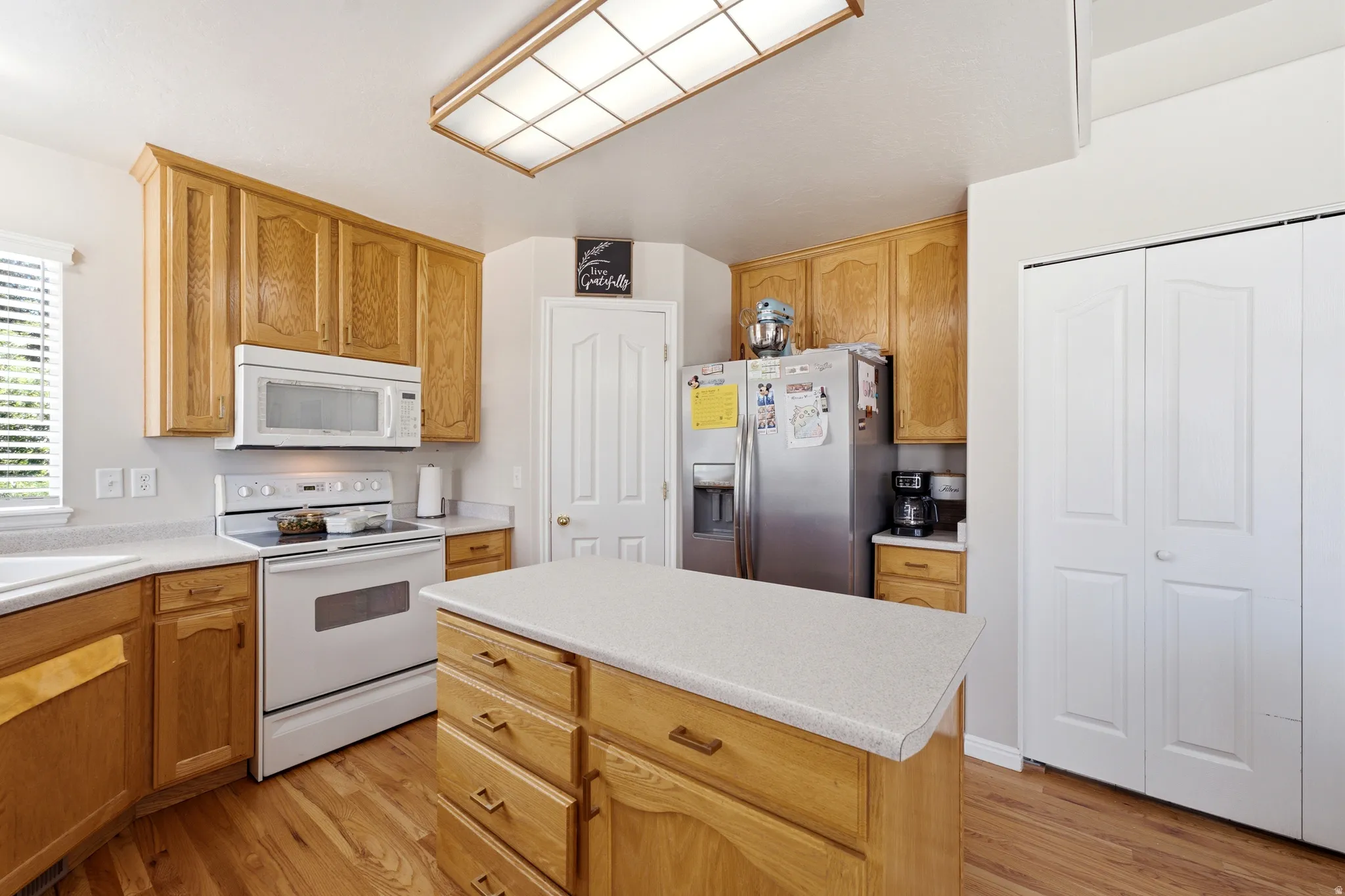 Kitchen featuring wood-finish flooring, wood cabinetry, white countertops, and white appliances