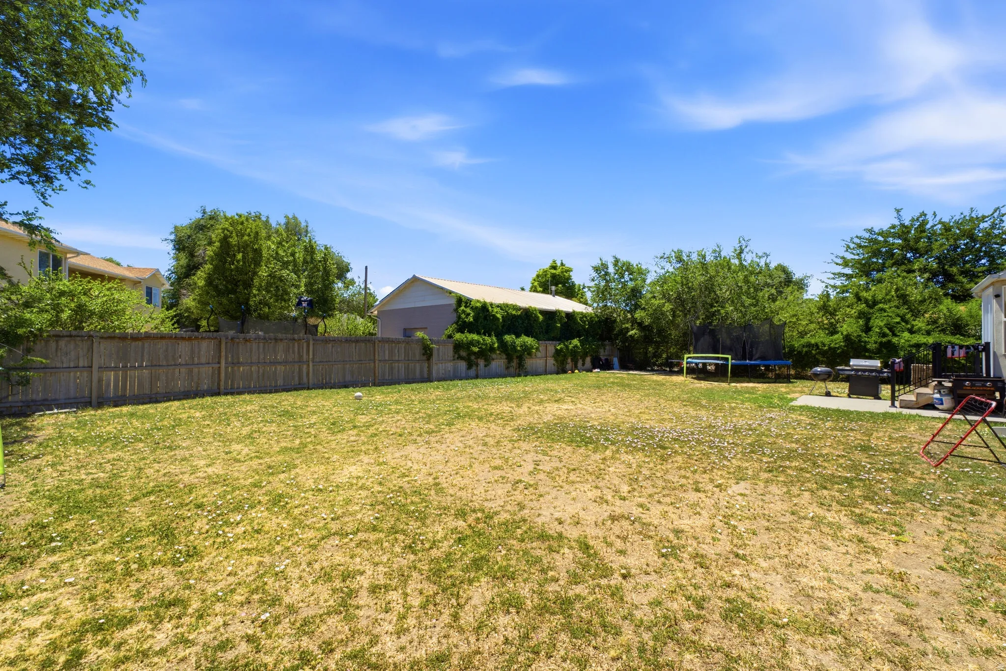 Expansive backyard featuring a wood fence, mature trees, and a detached structure