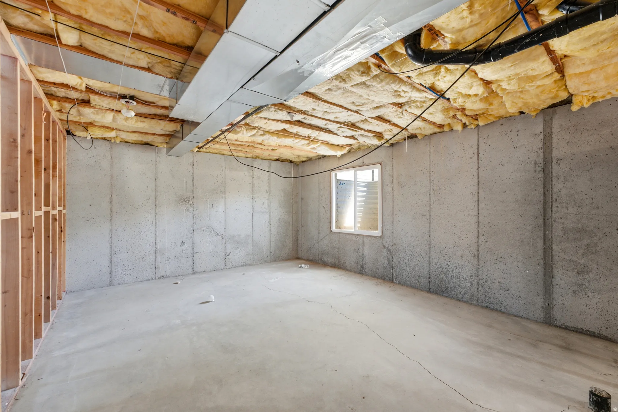 Unfinished lower level featuring exposed concrete walls and flooring, a single window, and visible ceiling insulation