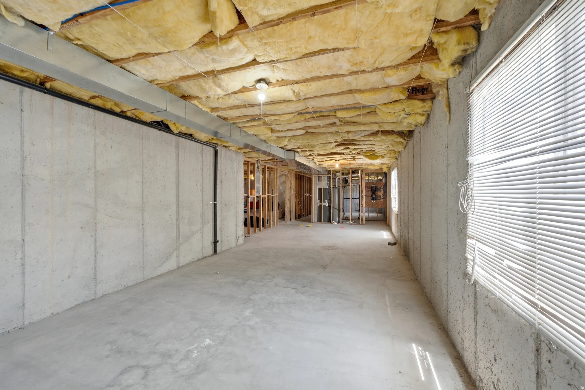 Unfinished basement offering expansive concrete flooring, exposed ceiling insulation, visible ductwork, and framed interior walls