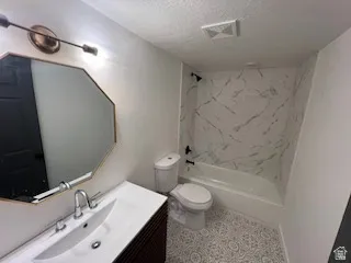 Bathroom featuring a white bathtub with a marble-patterned surround, a white toilet, and patterned floor tiling