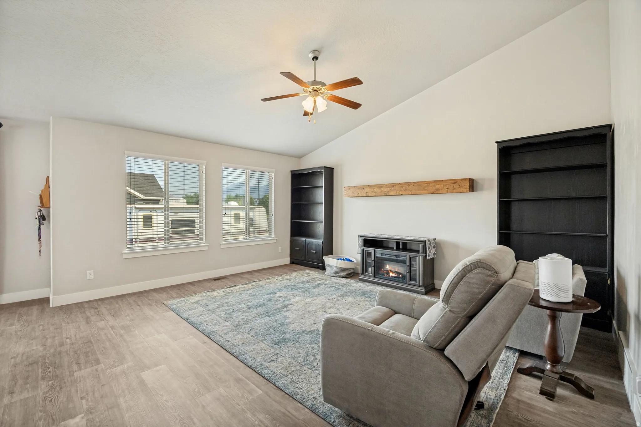 Vaulted ceiling great room featuring wood-finish flooring, an electric fireplace with a wood mantle, and two built-in shelving units