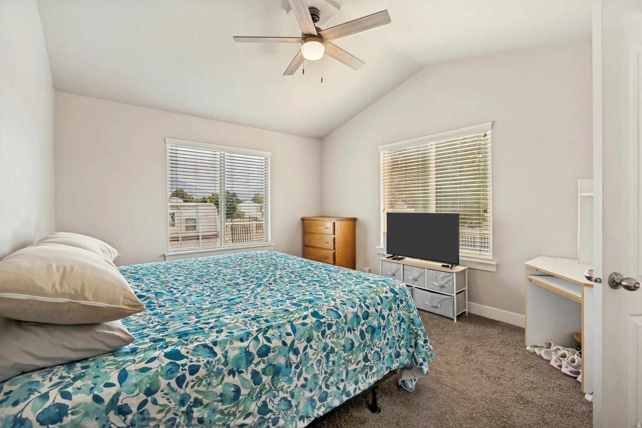 Vaulted ceiling bedroom featuring plush carpeting, two windows with horizontal blinds, and a ceiling fan with integrated lighting