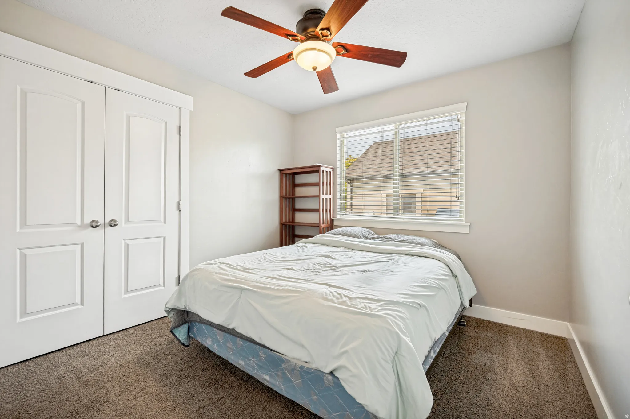 Carpeted room featuring a ceiling fan with light fixture, window with blinds, and white bi-fold closet doors