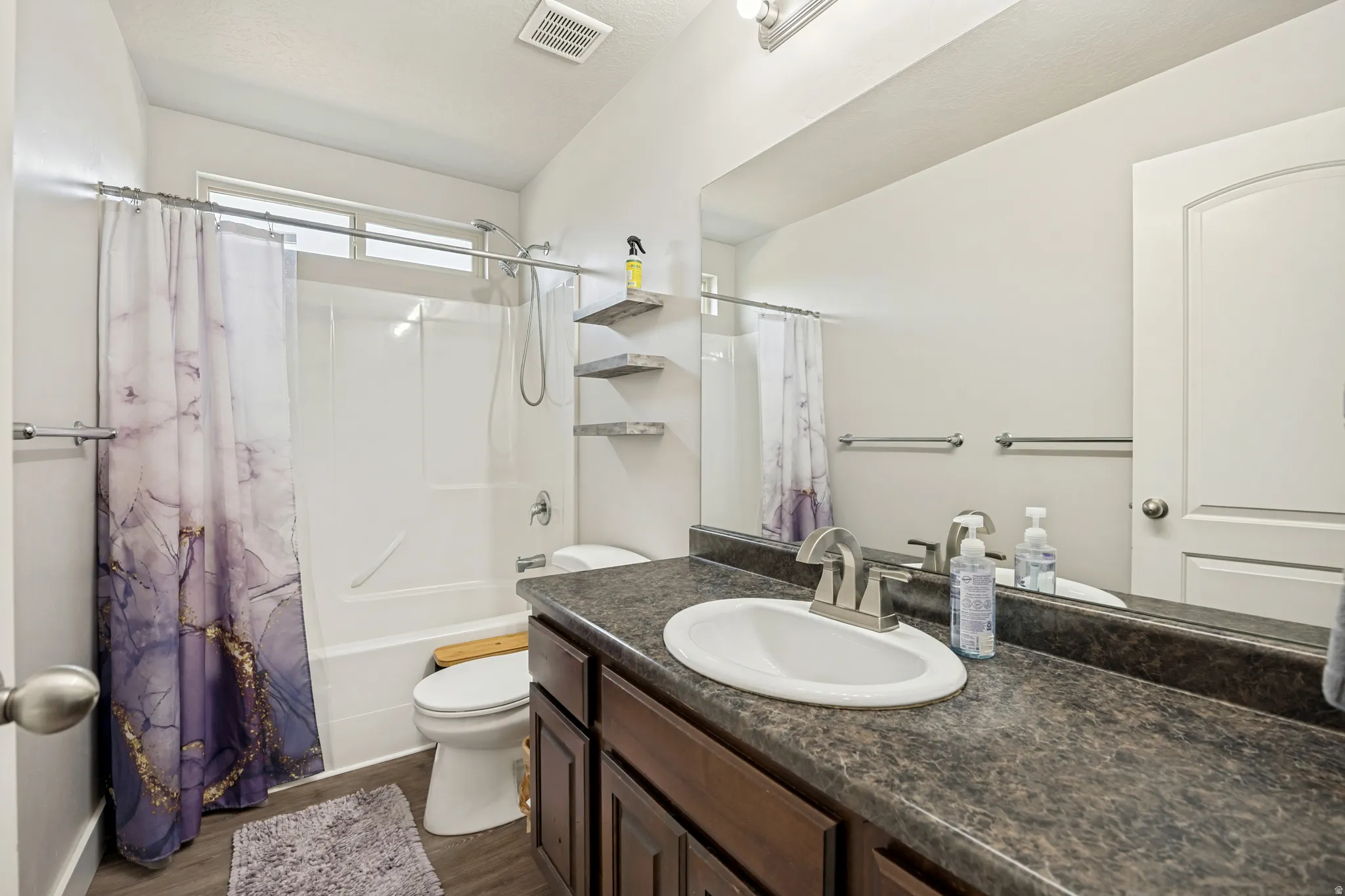Bathroom featuring a single vanity with a dark countertop, an integrated oval sink, and wood-finish cabinetry