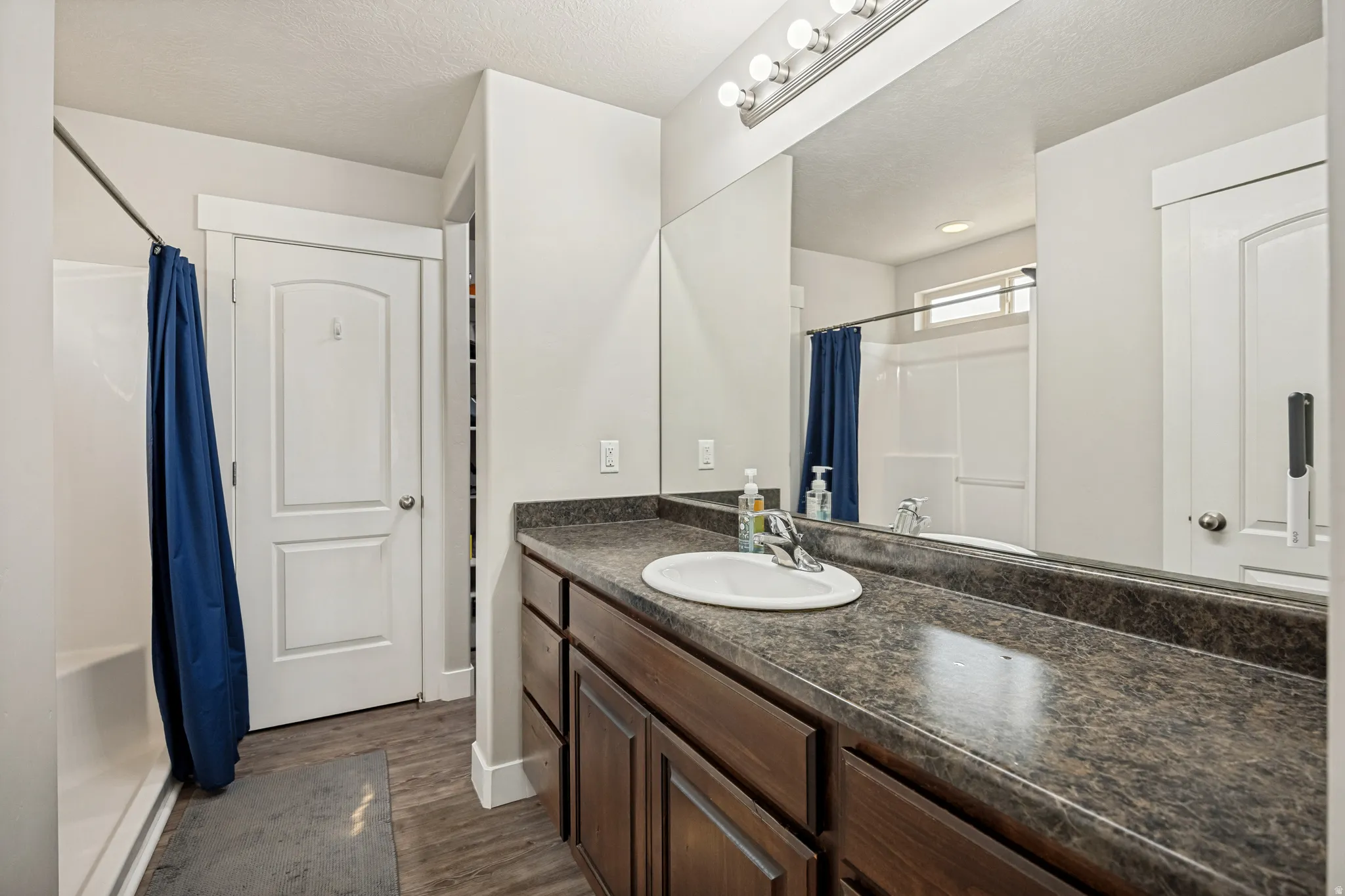 Bathroom featuring a vanity with a single basin sink, dark wood-finish cabinetry, a large wall-mounted mirror, and a shower-over-tub combination with a window