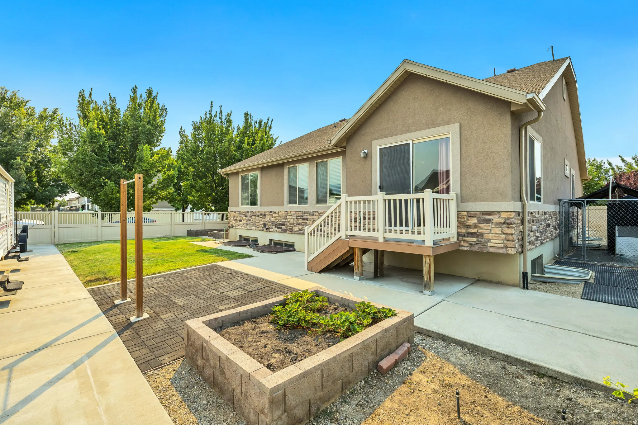Rear exterior featuring a multi-level deck with white railings, stone veneer accents, stucco siding, and a sliding glass door