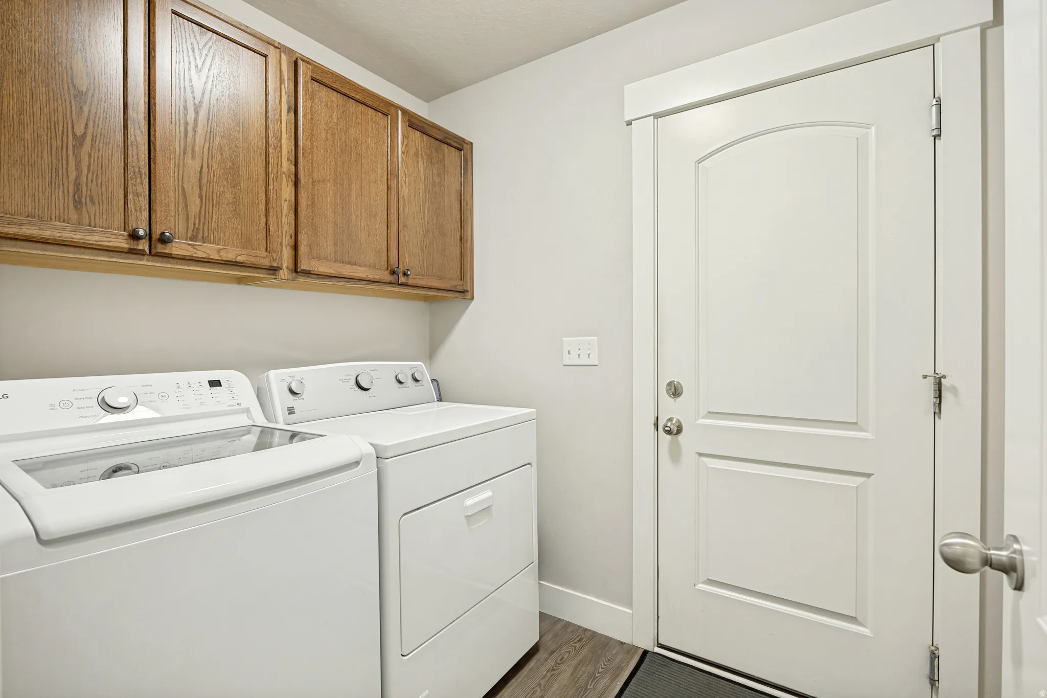 Laundry area featuring wood-finish upper cabinetry, a white paneled door with an arched top panel, and wood-finish flooring