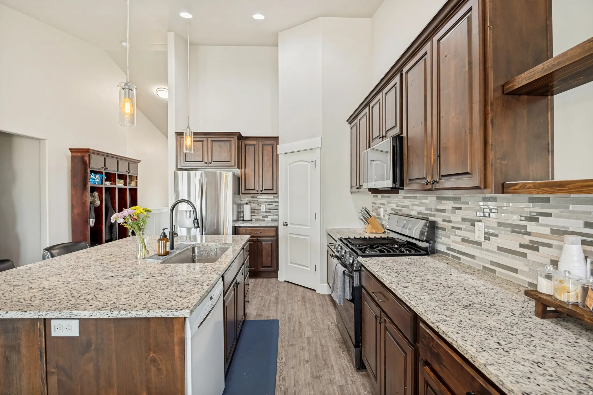 Spacious kitchen featuring an expansive island with an undermount sink, granite countertops, wood-finish cabinetry, stainless steel appliances, and a mosaic tile backsplash