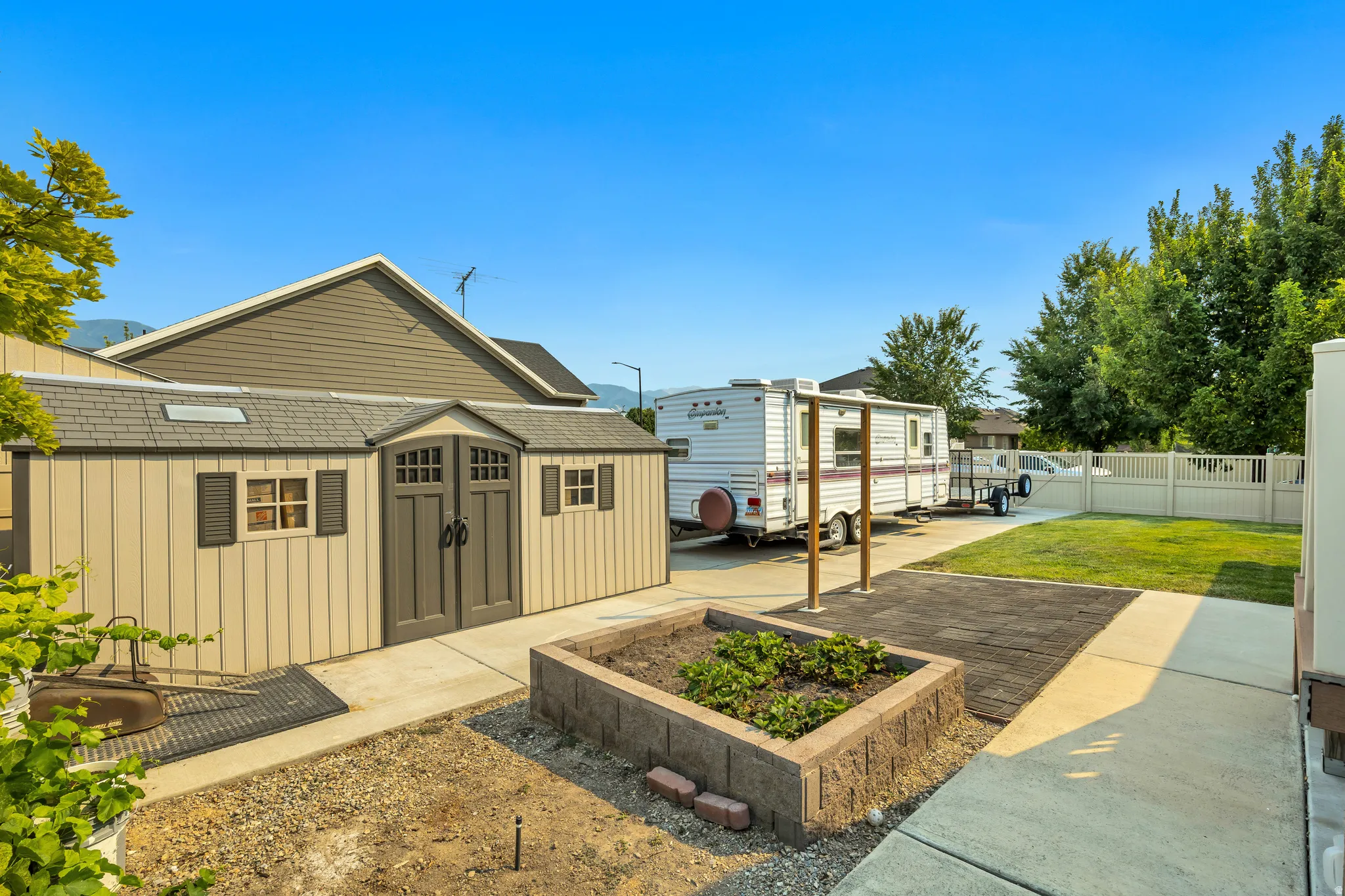 Expansive backyard featuring a large shed with double doors and window shutters, a raised garden bed, concrete pathways, and a partial privacy fence