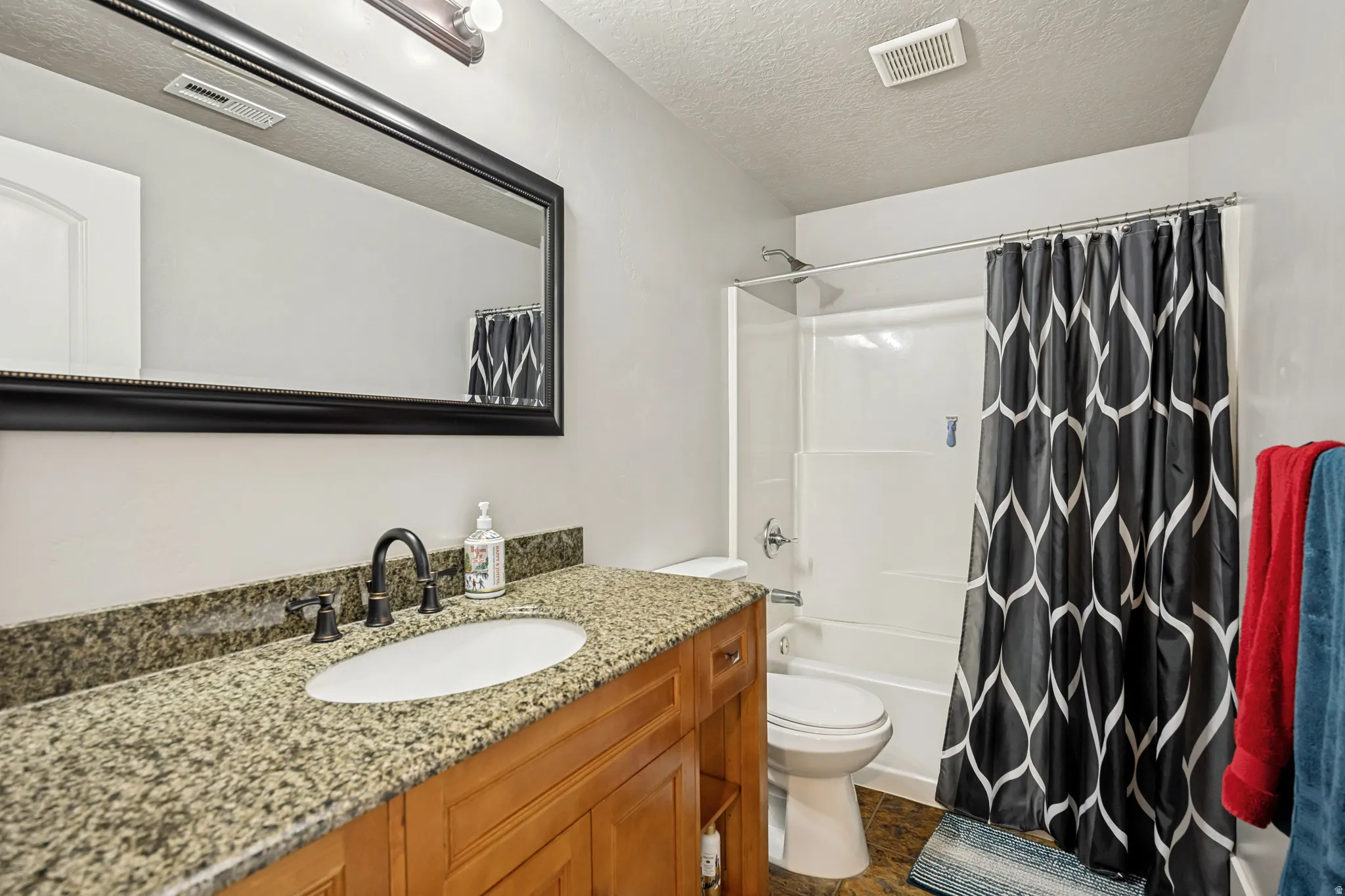 Bathroom featuring a wood-finish vanity with an oval undermount sink and a dark-toned countertop