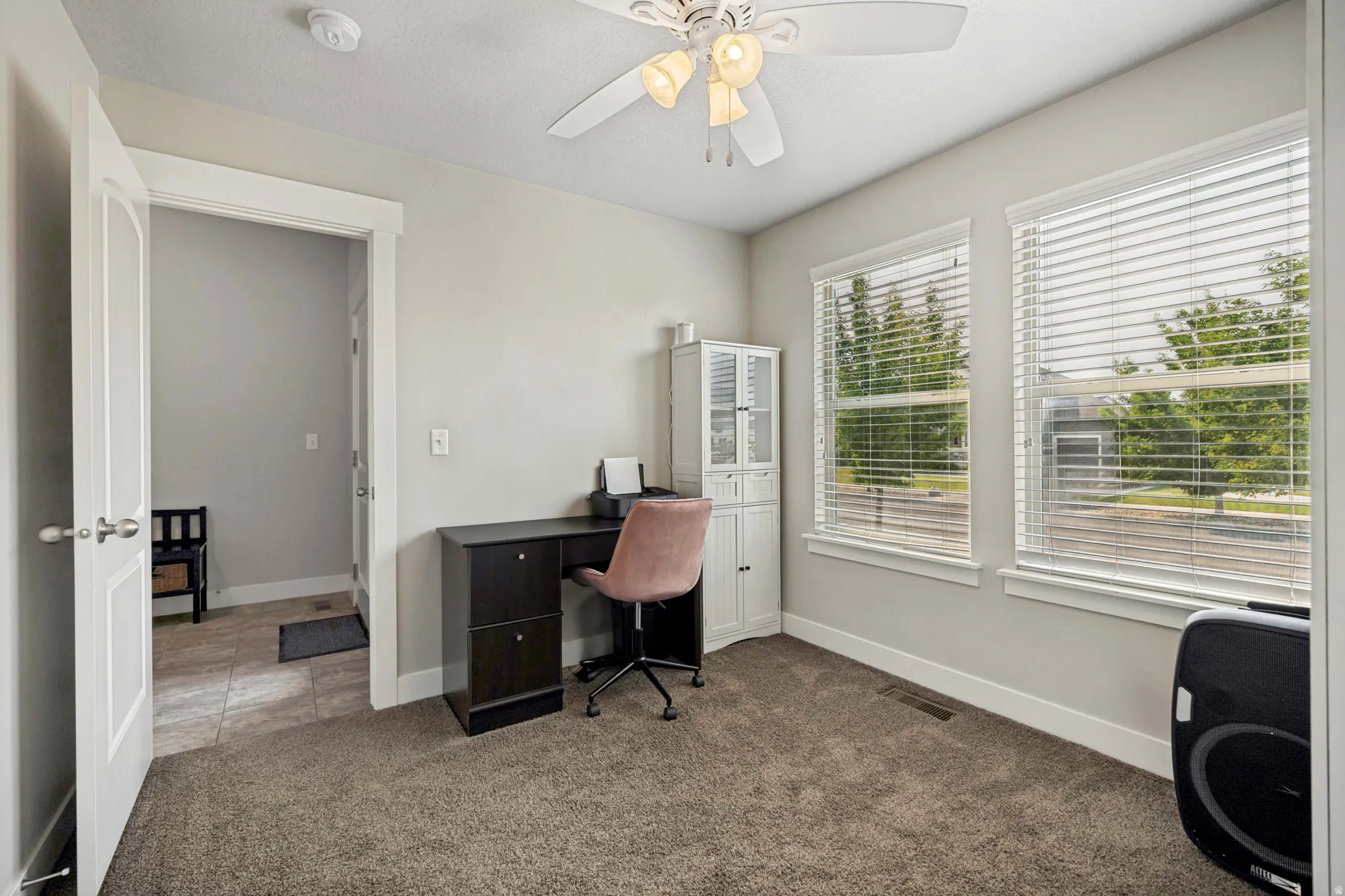 Carpeted room featuring two windows with horizontal blinds, a ceiling fan with integrated lighting, and a white paneled door with brushed nickel hardware