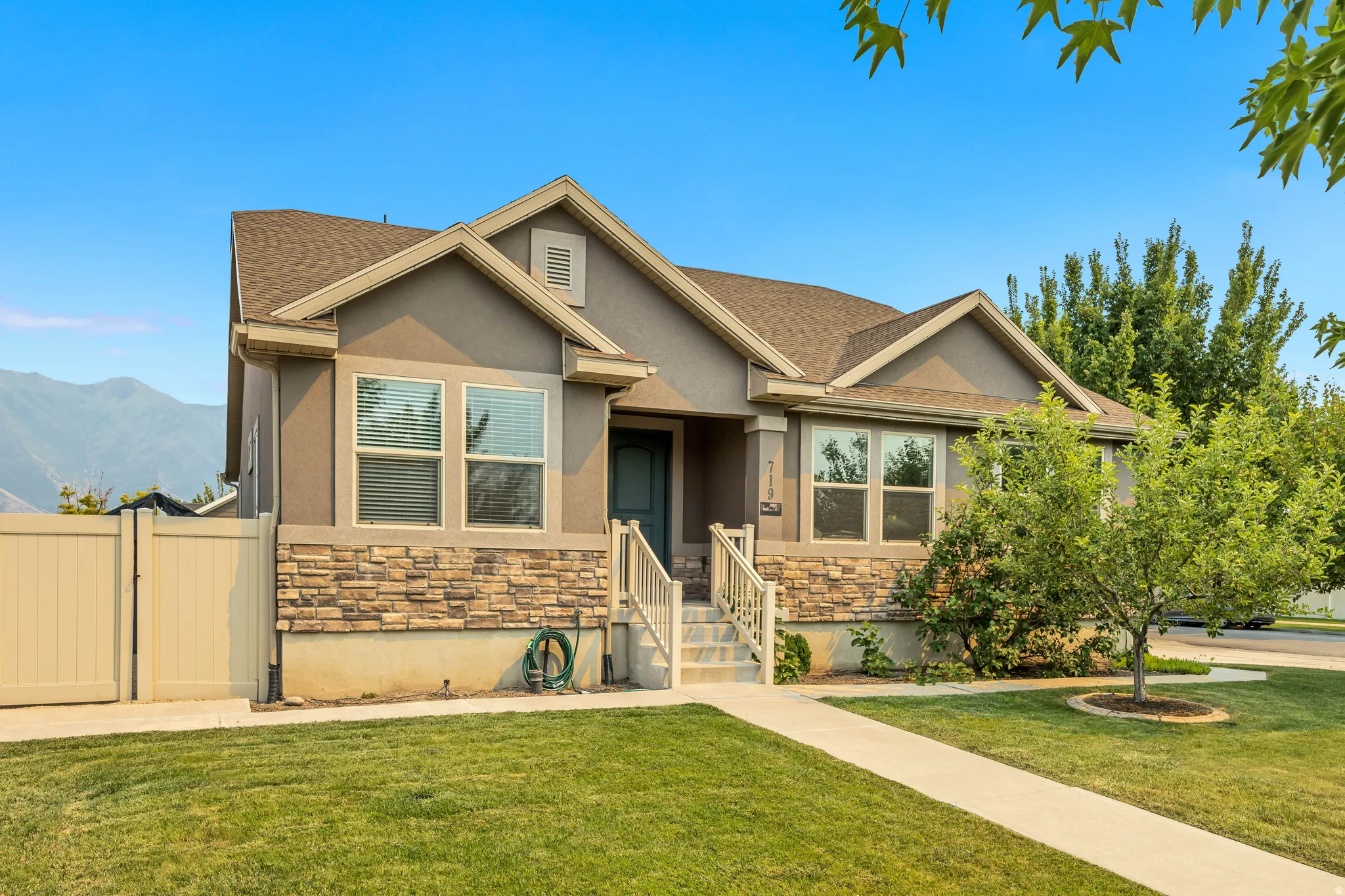 Exterior featuring a neutral stucco finish, stone veneer accents, a gabled roofline, and a prominent front walkway