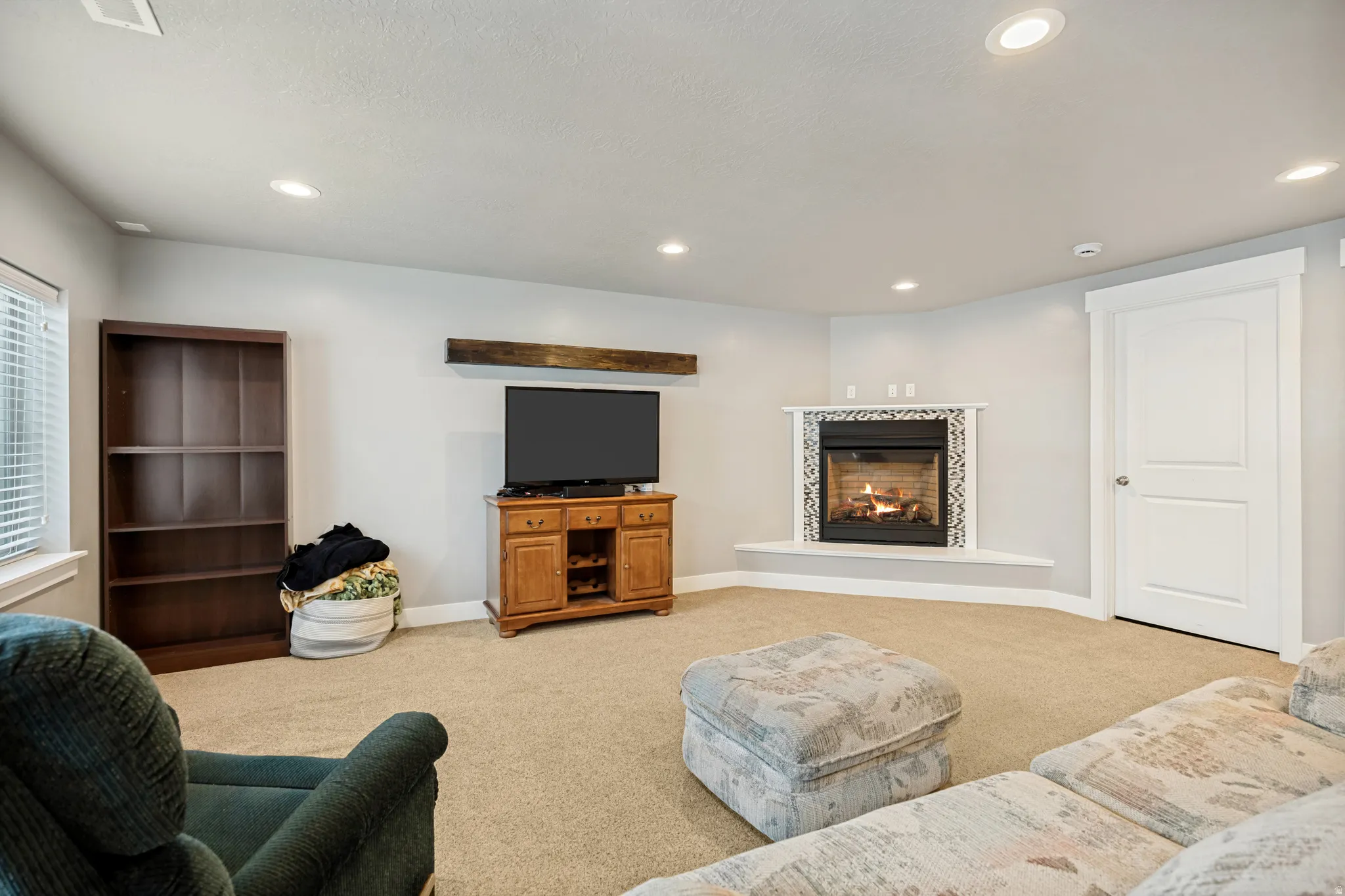 Recessed lighting illuminates this carpeted living area, featuring a corner fireplace with mosaic tile surround and a wood mantel