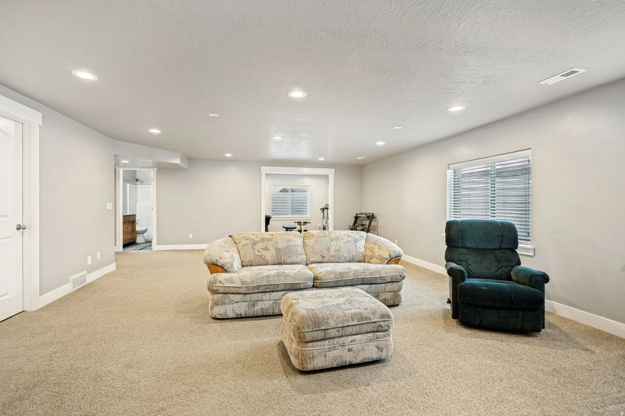 Spacious carpeted room featuring recessed lighting, a window with horizontal blinds, and neutral-toned walls