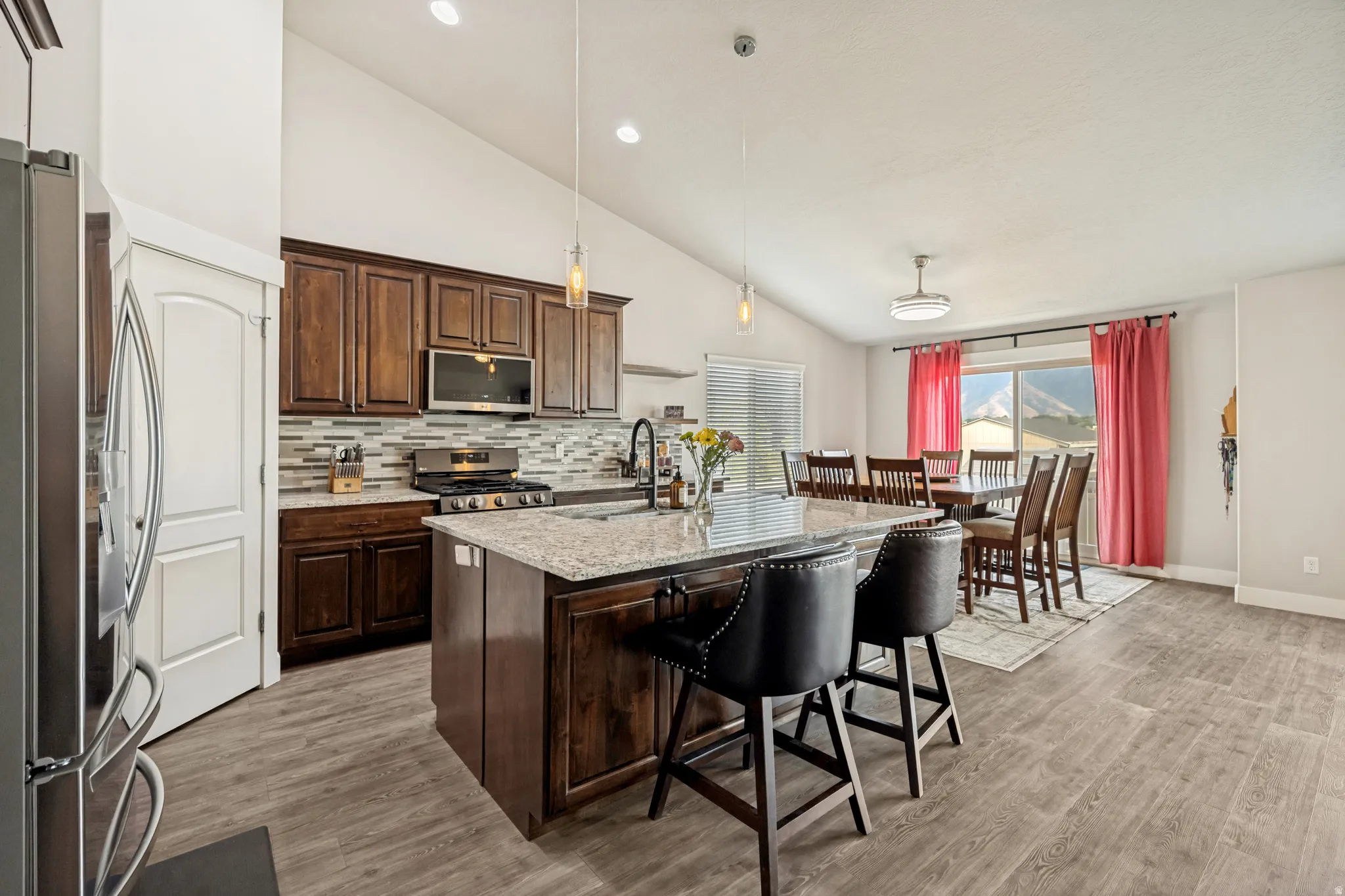 Open-concept kitchen featuring dark wood cabinetry, stainless steel appliances, a tile backsplash, and a central island with a granite-style countertop
