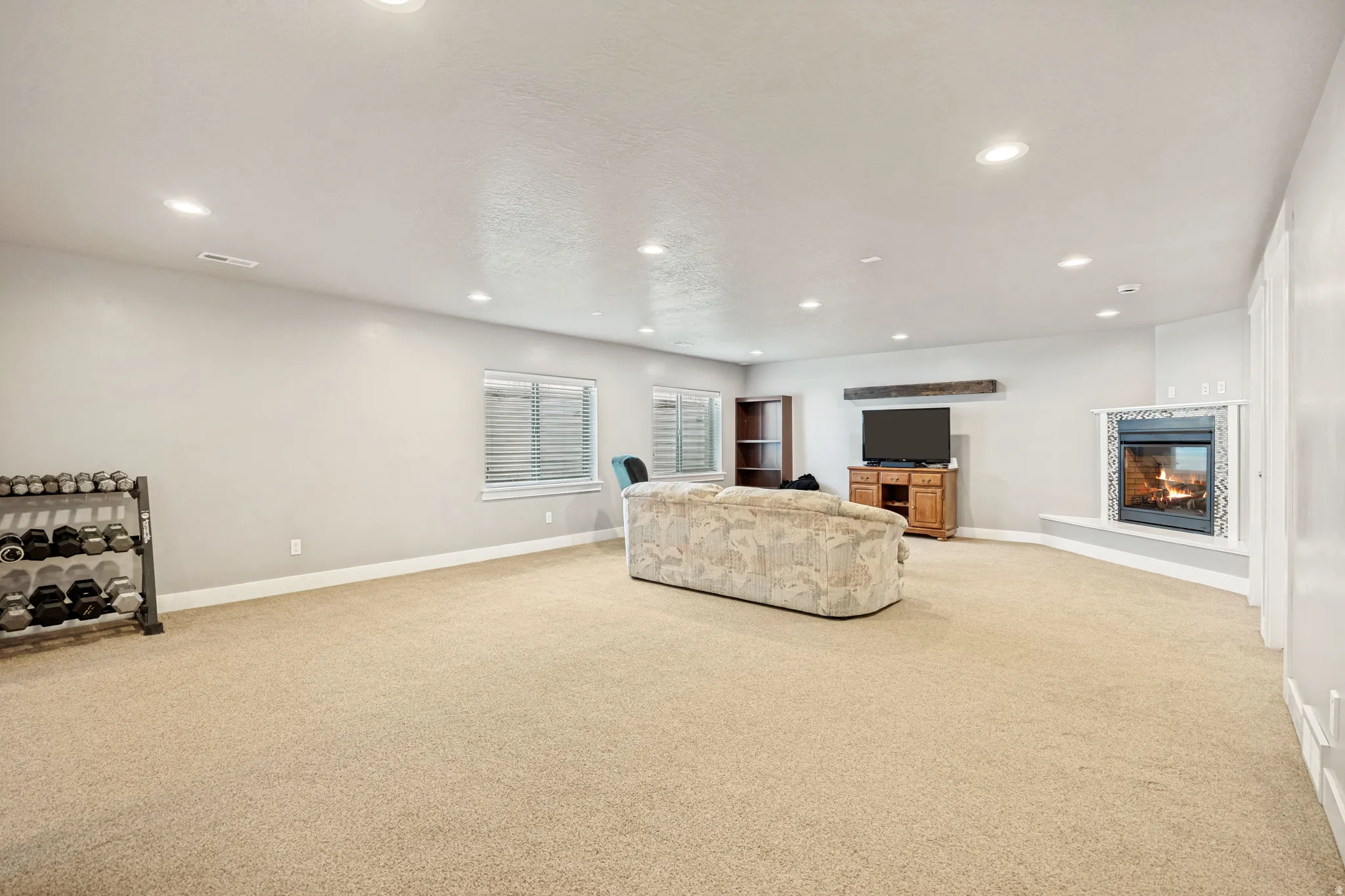 Spacious room featuring neutral carpeting, recessed lighting, and a fireplace with a decorative mantel and hearth