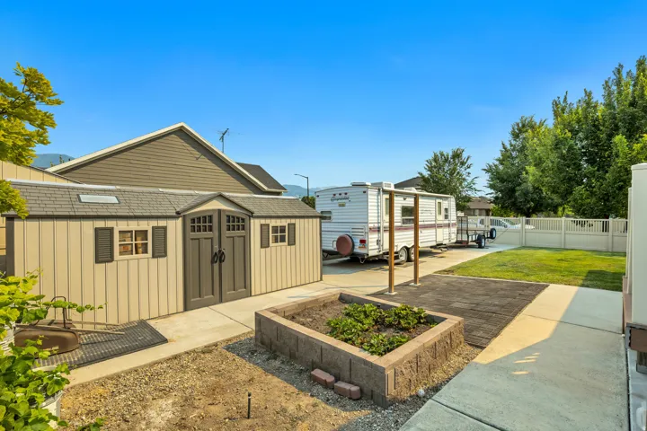 Expansive backyard featuring a large shed with double doors and window shutters, a raised garden bed, concrete pathways, and a partial privacy fence