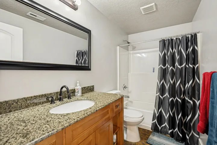 Bathroom featuring a wood-finish vanity with an oval undermount sink and a dark-toned countertop