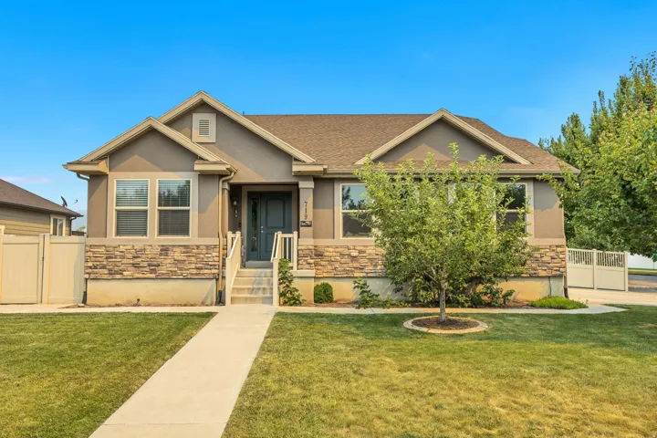 Exterior featuring a stucco finish, stone veneer facade, a dark gray entry door, concrete pathway, and a manicured lawn