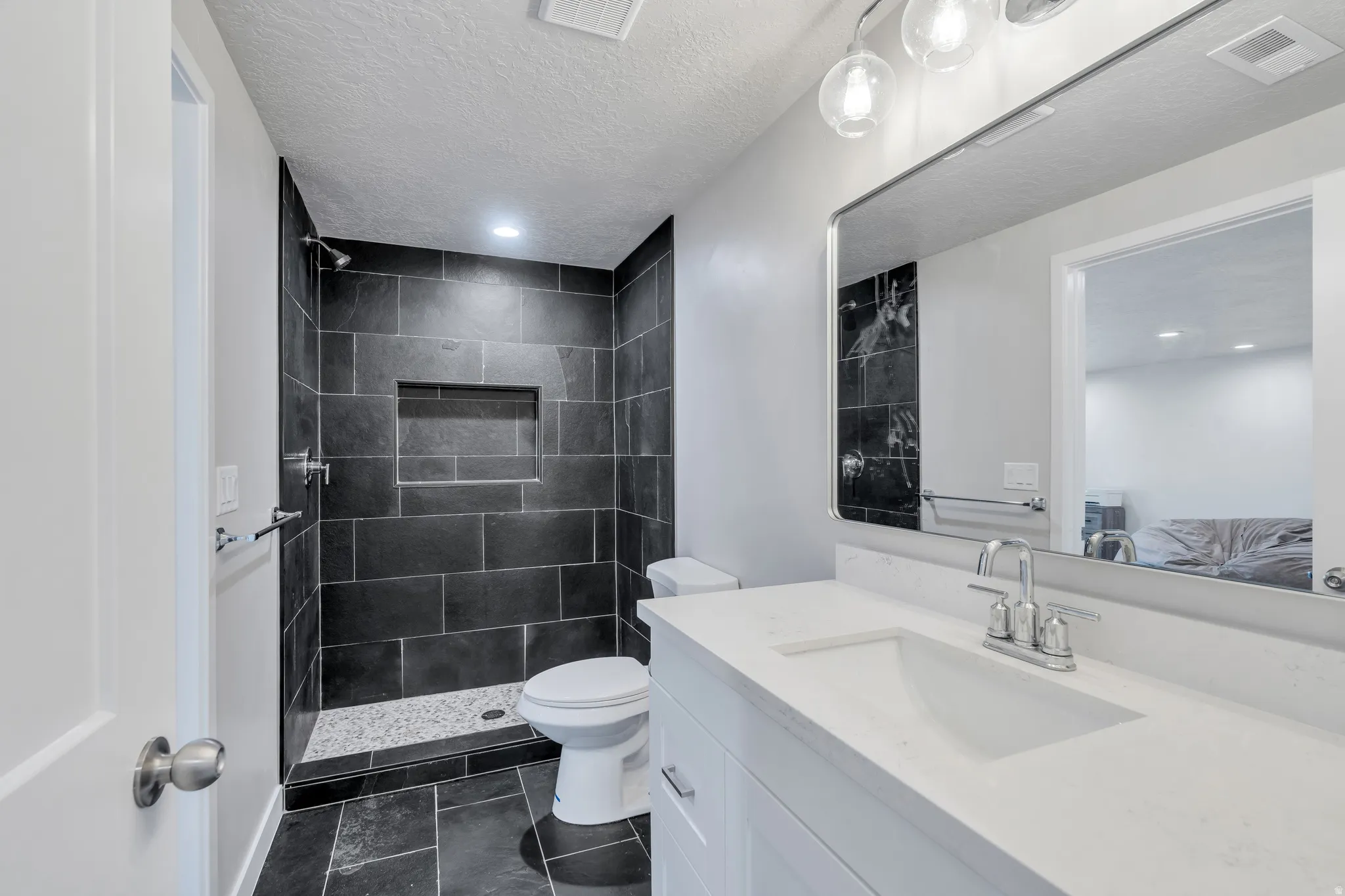 Modern bathroom featuring a walk-in shower with dark stone-look tile, a built-in shower niche, and a contrasting pebble-style shower pan