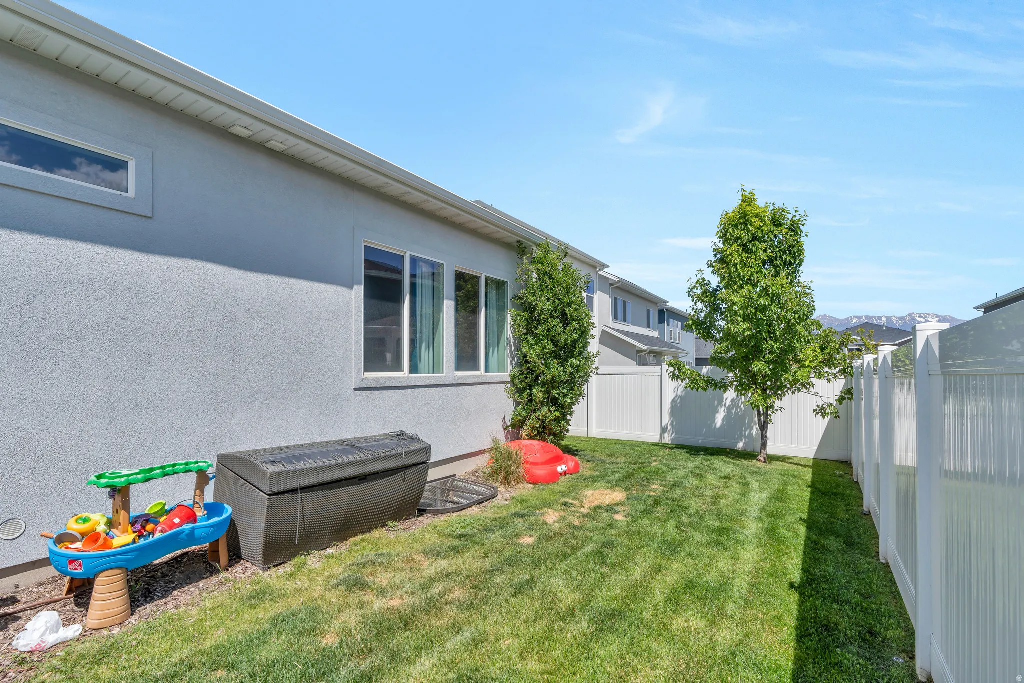 Fenced backyard featuring a manicured lawn, established trees, and white vinyl perimeter fencing