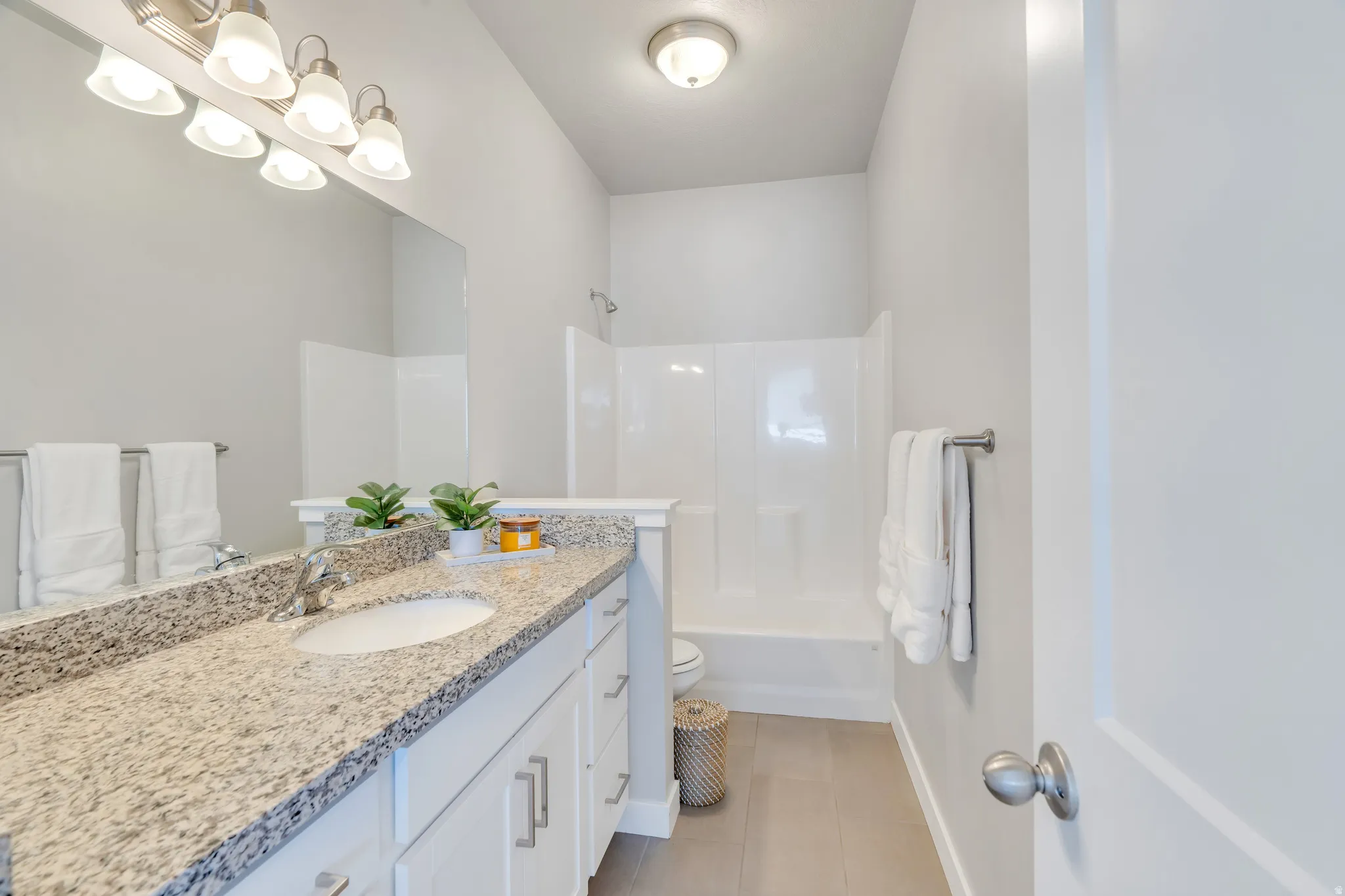 Spacious bathroom featuring a granite-style countertop, white cabinetry with silver hardware, a single undermount sink, and a built-in shower/tub combination