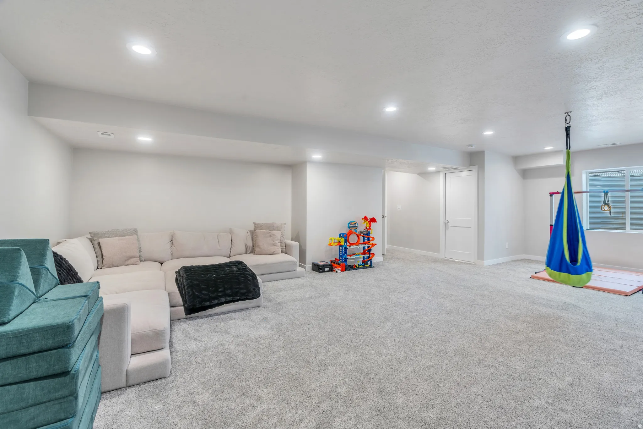Spacious lower-level room featuring light gray carpeting, recessed lighting, and white painted walls